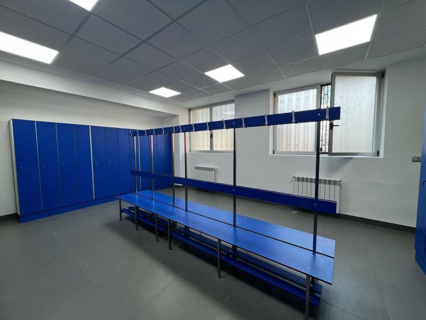 Vestuario con bancos fenólicos azules, percheros centrales y taquillas de gran capacidad en espacio deportivo o de empresa