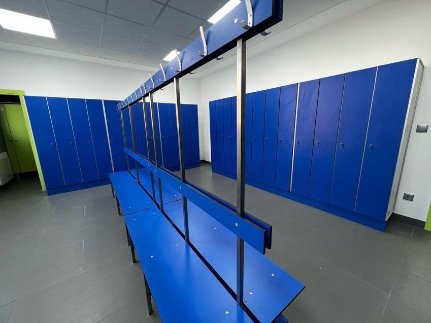 Vestuario con bancos fenólicos azules centrales y taquillas azules de gran capacidad en instalación deportiva o empresarial