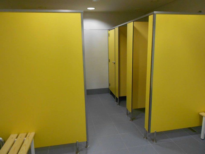 Cabinas fenólicas amarillas instaladas en vestuario colectivo con puertas compactas, perfilería de aluminio y suelo cerámico gris