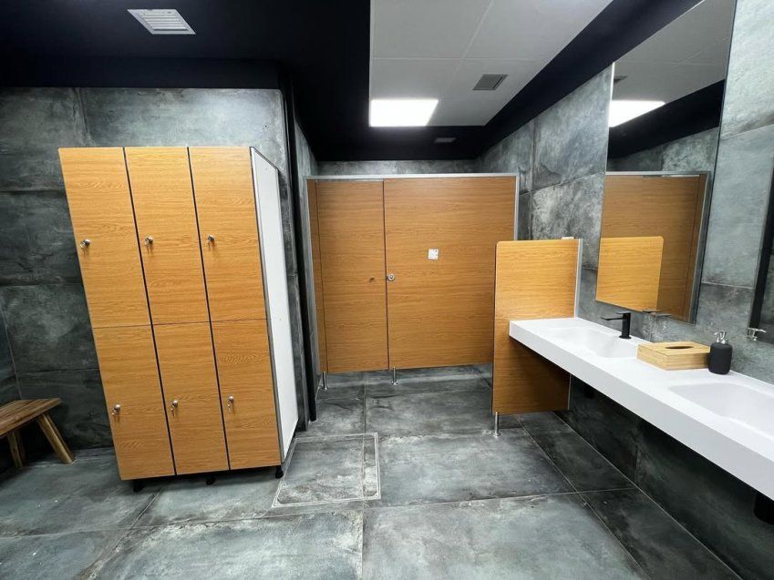 Vestuario moderno con taquillas fenólicas acabado madera, cabinas sanitarias y lavabo blanco en espacio de diseño contemporáneo