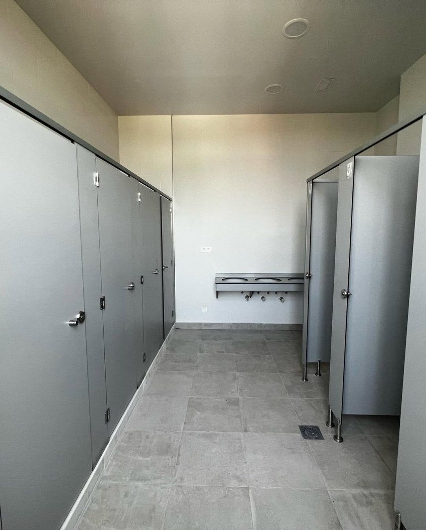 Cabinas fenólicas grises instaladas en zona de aseos y vestuarios con lavabos, suelo antideslizante y perfilería metálica